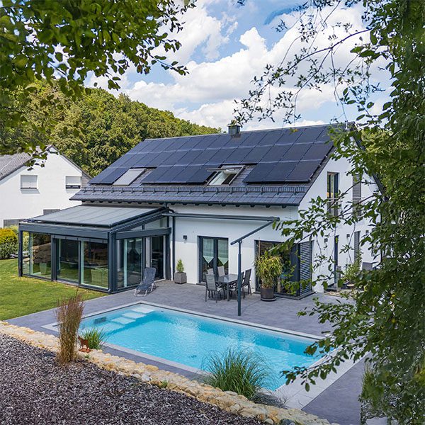 Ein weißes Einfamilienhaus mit Garten und Pool. Auf dem Dach sind vollflächig Solarmodule installiert.