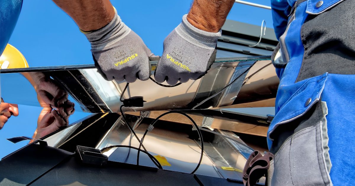 Nahaufnahme von Technikern, die Kabel an der Rückseite eines Solarmoduls anschließen — gut sichtbar die transparente Glas-Glas-Struktur bifazialer Module