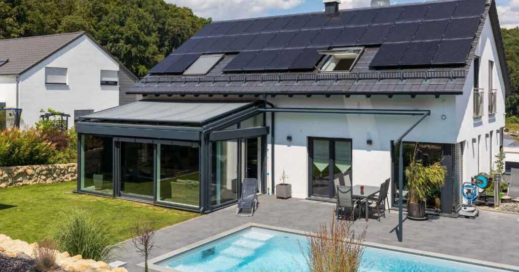 Ein modernes Einfamilienhaus in Frontalansicht mit einer Photovoltaikanlage auf dem Dach und einem Pool im Garten.