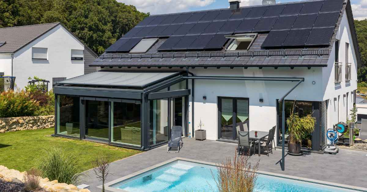 Ein modernes Einfamilienhaus in Frontalansicht mit einer Photovoltaikanlage auf dem Dach und einem Pool im Garten.